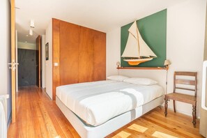 A bedroom with a wooden floor, a bed with white bedding, a wooden chair, a wall-mounted sailboat decoration, and a green accent wall. - Casa Azevinho - Caniçada Gêres (Vieira do Minho)