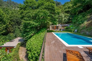 A wooden deck with a swimming pool, surrounded by lush greenery and a hillside. - Casa Azevinho - Caniçada Gêres (Vieira do Minho)