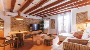 A cozy living room with a stone wall, wooden beams, a TV, a sofa, and a dining area. - Bravissimo Calderers El Cavall, in the Barri Vell (Girona)