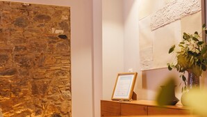 A reception area with a stone wall, a wooden desk with a framed sign, and a potted plant. - Bravissimo Calderers El Cavall, in the Barri Vell (Girona)