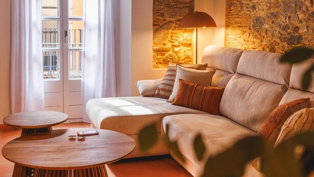 A cozy living room with a sofa, two round wooden tables, and a stone wall. - Bravissimo Calderers El Cavall, in the Barri Vell (Girona)