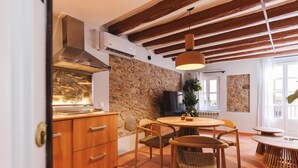A cozy dining area with a round wooden table, wicker chairs, and a stone wall. - Bravissimo Calderers El Cavall, in the Barri Vell (Girona)
