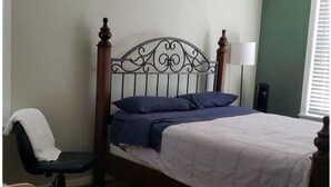 A neatly made bed with a headboard, a bedside lamp, and a chair with a blanket.