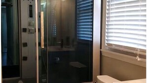 A bathroom with a glass partition, a toilet, and a window with blinds.