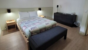 Un dormitorio con cama, mesitas de noche, un banco, cómoda y lámpara de techo.