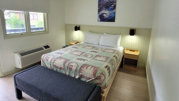 Un dormitorio con una cama, dos mesitas de noche, un banco, un radiador y una ventana.