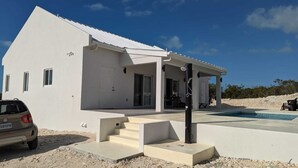 Ein modernes, weißes Haus mit überdachter Terrasse und Swimmingpool.