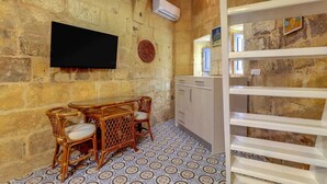 Une pièce aux murs de pierre, dotée d’un téléviseur à écran plat fixé au mur, de meubles en osier, d’un sol à motifs et d’une étagère blanche.