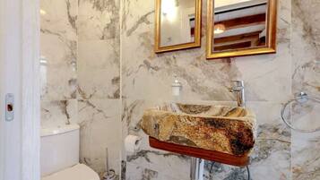 A bathroom with a marble wall, a sink with a unique stone countertop, and two mirrors with gold frames.
