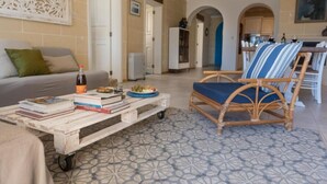 Un soggiorno con un divano, un tavolino da caffè con libri e una bottiglia, una poltrona in vimini e un pavimento decorato.