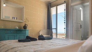 Una camera d'albergo con un letto, una cassettiera, una sedia e vista sul mare attraverso una grande finestra.