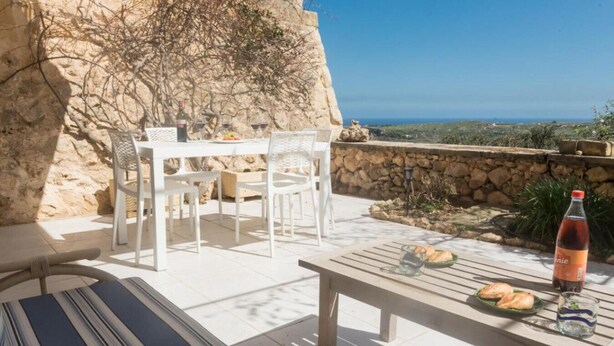 Una terrazza con un tavolo apparecchiato per due persone, una bottiglia di bevanda e vista sul paesaggio.