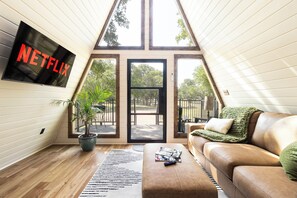 Een gezellige woonkamer met een grote televisiescherm waarop 'NETFLIX' staat, een potplant, een bruine leren bank en een raam met uitzicht op een tuin.