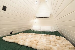 A room with a sloped ceiling, a bed with a green bedspread, a fluffy beige blanket, and a white pillow. - Intimate A Frame*Hot Tub*Near Hiking & Stockyards (Fort Worth)