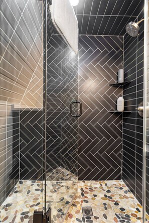 A shower with a herringbone tile pattern and a pebble-tiled floor. - Intimate A Frame*Hot Tub*Near Hiking & Stockyards (Fort Worth)