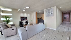 A modern living room with a grey sofa, a flat-screen TV, and a potted plant. - Cozy oceanfront condominium-2 bed in main street, 1 block away from ferry. (Cozumel)