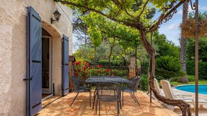 Eine Terrasse mit Tisch und Stühlen, ein Schwimmbad und ein Garten mit roten Blumen und einem Baum.