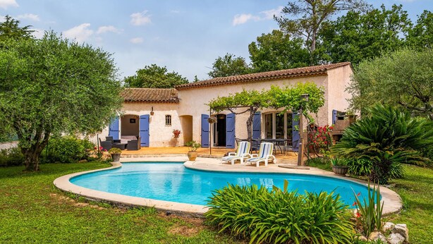 Eine Villa mit Swimmingpool, Sitzgelegenheiten im Freien und üppiger Bepflanzung.