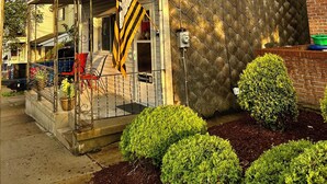 A two-story house with a porch, a brick wall, and a chain-link fence.