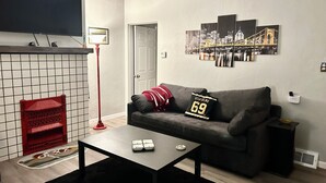 A modern living room with a grey sofa, a coffee table, a red floor lamp, and a cityscape artwork on the wall.