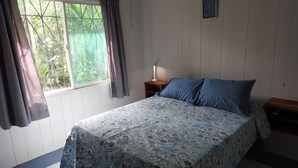 Een slaapkamer met een bed, nachtkastje, raam met gordijnen en een airconditioning.