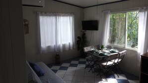 Een kamer met een geruite vloer, een eettafel met stoelen, een plafondventilator, een aan de muur bevestigde televisie en een raam met gordijnen.
