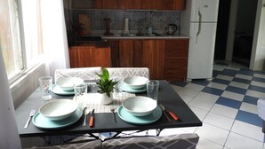 Een eethoek met een tafel gedekt voor vier personen, een keuken op de achtergrond en een geruit vloertje.