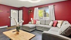 Un salon moderne avec un canapé d’angle, une table basse en bois et une grande fenêtre agrémentée de rideaux.
