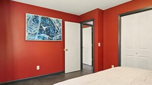 Une chambre avec des murs rouges, une porte blanche et un grand tableau abstrait accroché au mur.