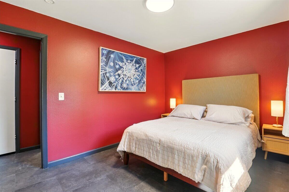 Une chambre d’hôtel avec un mur rouge, un grand lit avec une literie blanche, une tête de lit en bois et une table de chevet avec une lampe.
