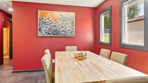 Une salle de conférence avec une table en bois, des chaises beiges, un tableau au mur et de grandes fenêtres.