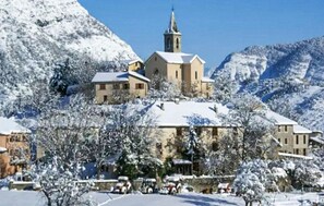 Un pueblo cubierto de nieve con una iglesia en una colina, rodeado de montañas.