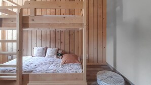 Een stapelbed met houten frame en een matras met een bloemenprint. Er liggen kussens met tekst op en een teddybeer op het bed.