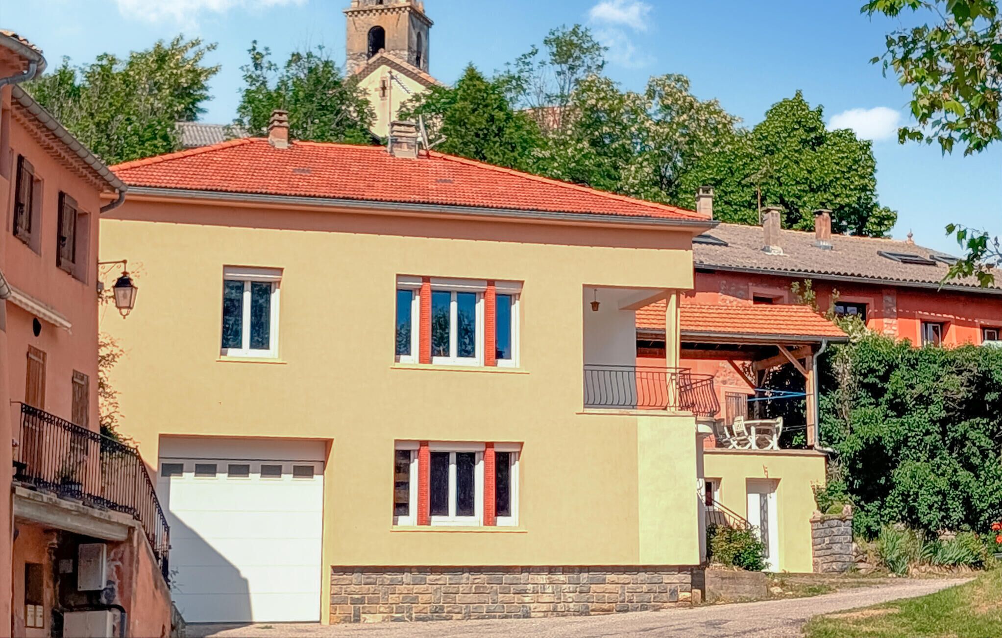 Un bâtiment à deux étages, doté d’un toit recouvert de tuiles rouges, d’une porte de garage blanche et d’un petit balcon avec une rambarde en métal.