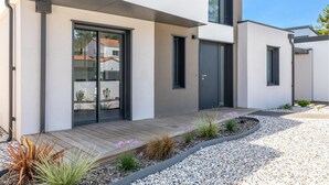 Ein modernes Haus mit einer Holterrasse, einem Kiesweg und verschiedenen Pflanzen.