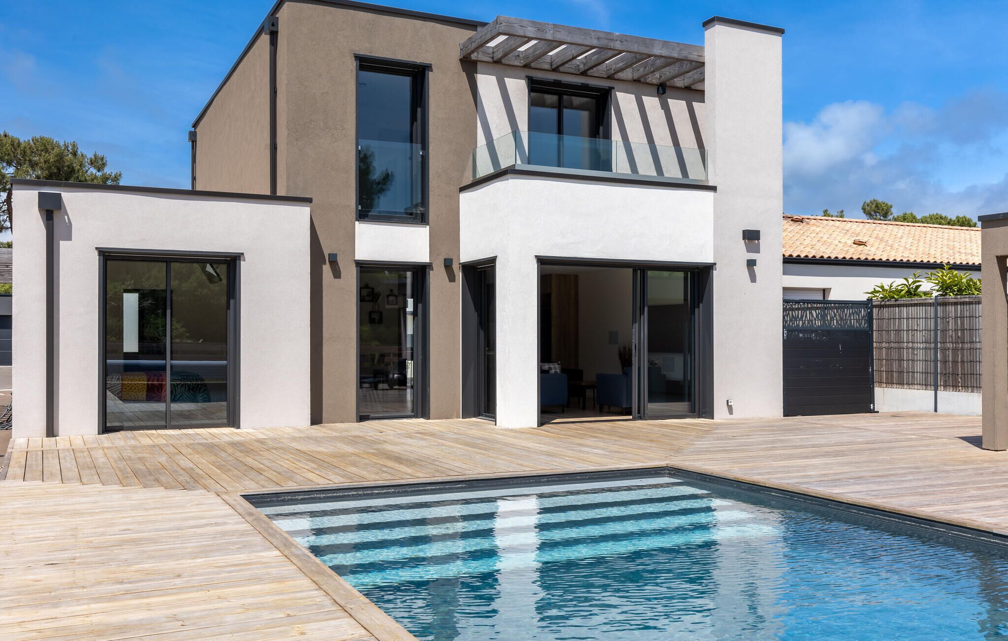 A modern two-story house with a swimming pool, large glass windows, and a wooden deck.
