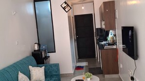 Een moderne woonkamer met een blauwgroene bank, een salontafel en een aan de muur bevestigde televisie. In de achtergrond is een keuken te zien.
