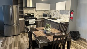 Una cocina moderna con un refrigerador de acero inoxidable, estufa, microondas y pileta. Hay una mesa de comedor con sillas y una pequeña planta en maceta.