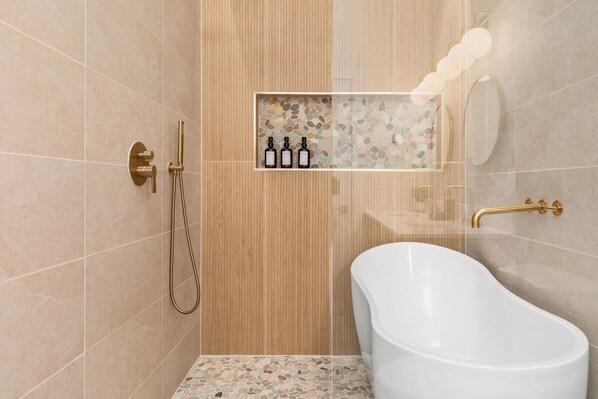 Un baño moderno con una bañera independiente, una ducha con grifo dorado y un estante con tres botellas.