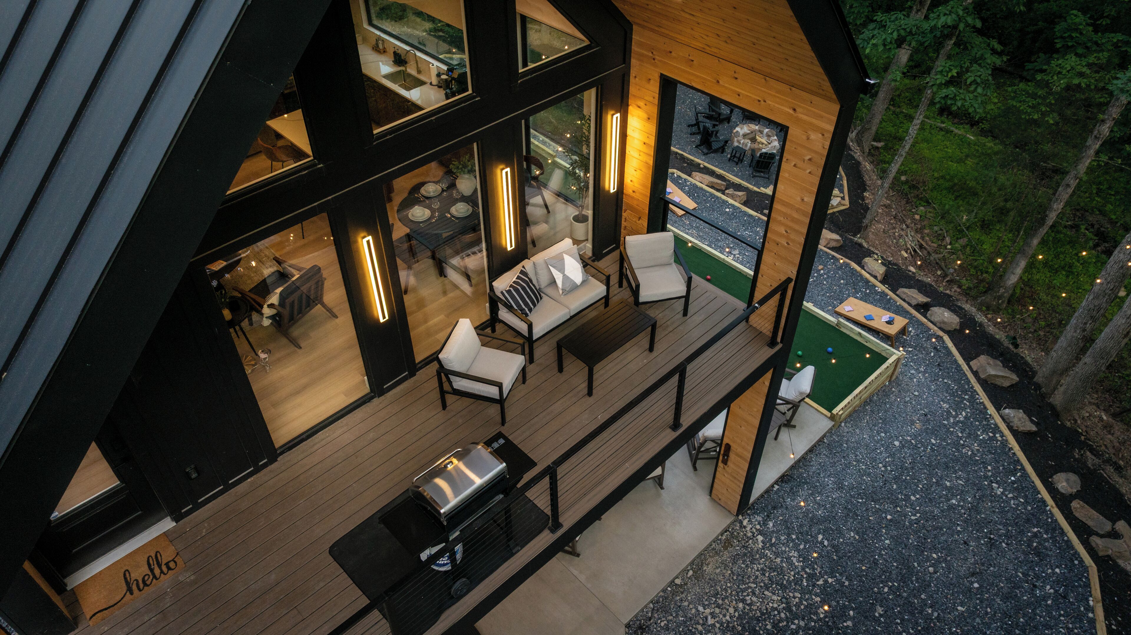A modern house with a deck, outdoor seating, and a view of the surrounding forest.