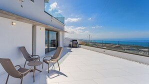 Un balcón moderno con mobiliario exterior, una puerta de cristal y vista al océano.