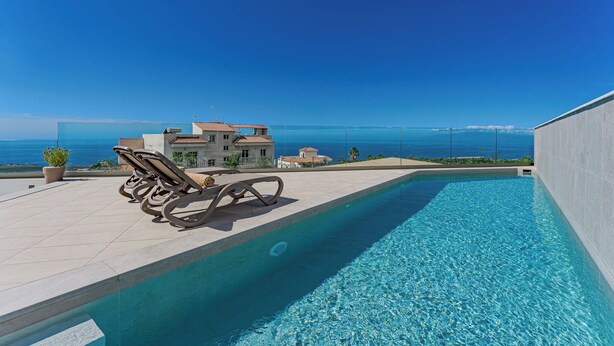 Una piscina con sillas de descanso, vista al mar y una casa al fondo.