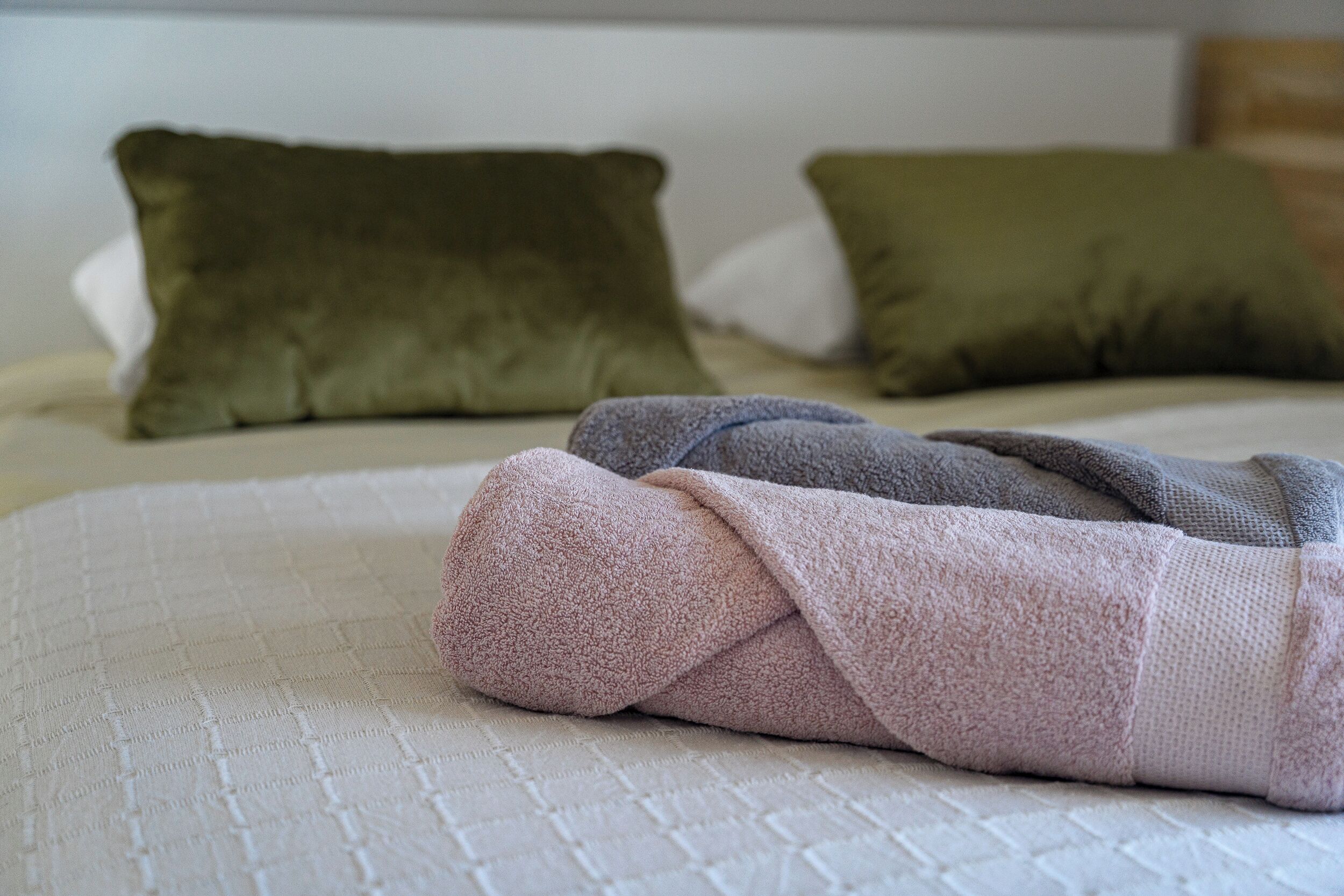 A neatly made bed with a quilted white cover, two green pillows, and a folded pink blanket.