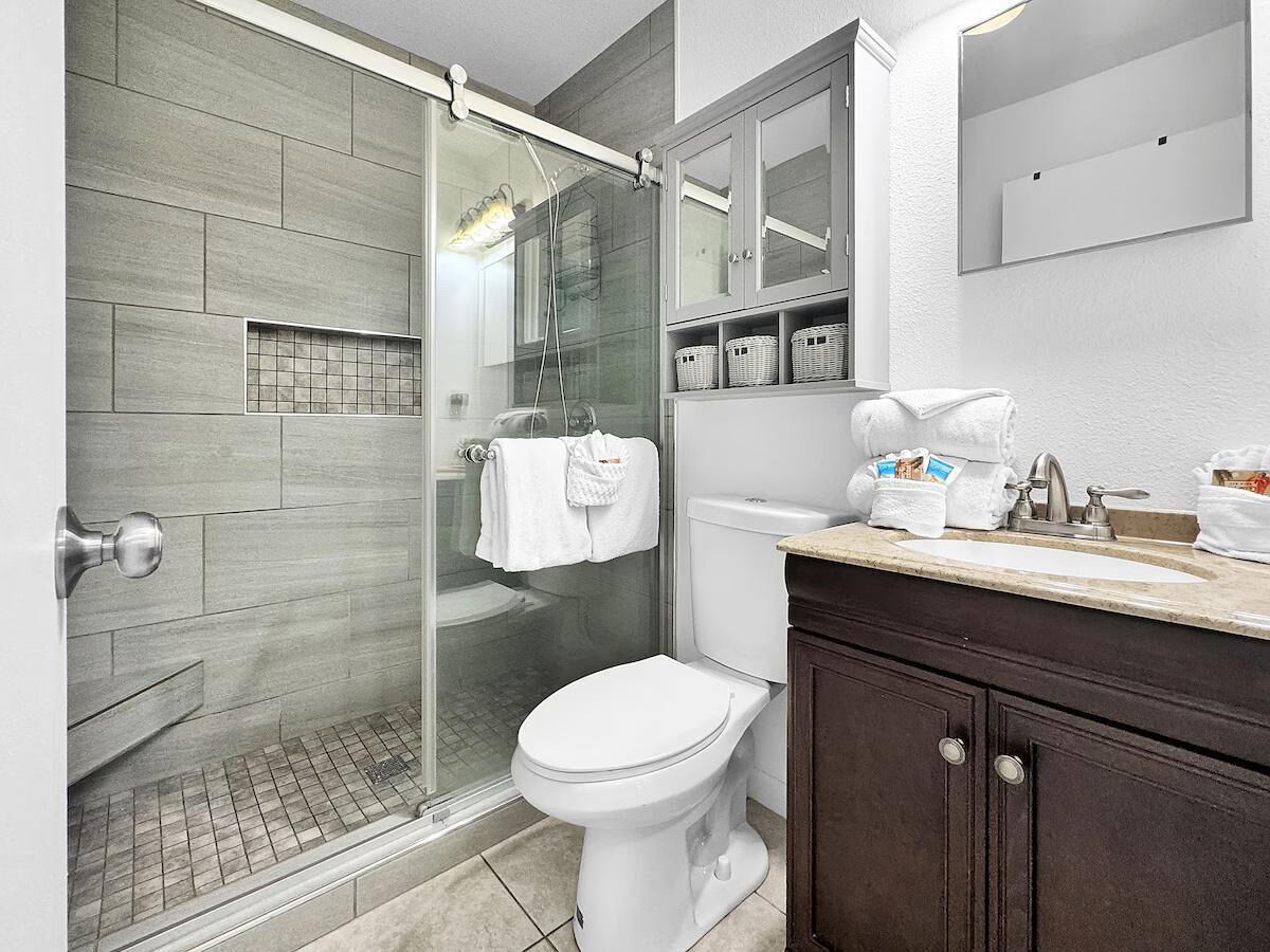 Ein modernes Badezimmer mit einer Duschkabine aus Glas, einer weißen Toilette und einem dunklen Holzwaschtisch mit Waschbecken.