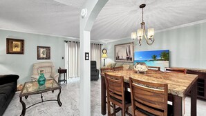 Amplia sala de estar con piso de mármol, comedor con mesa y sillas de madera, y un cuadro grande que representa una escena de playa.