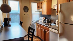 Une cuisine de taille réduite, dotée de meubles en bois, d’un réfrigérateur blanc, d’une cuisinière et d’une machine à café.
