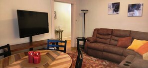 A living room with a brown sofa, a TV mounted on the wall, a round wooden table with candles, and a patterned rug. - Charming 2-bedroom apartment with equipped kitchen and AC, in Cumberland, MD. (Cumberland)