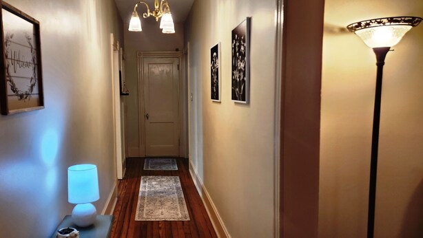 Un couloir doté d’un plancher en bois, d’un tapis, d’une lampe fixée au mur et de tableaux encadrés.