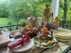 A table set with various food items, including bread, a salad, and a meat dish, on a balcony with a view of greenery. - Green River Bridge Inn (Guilford)