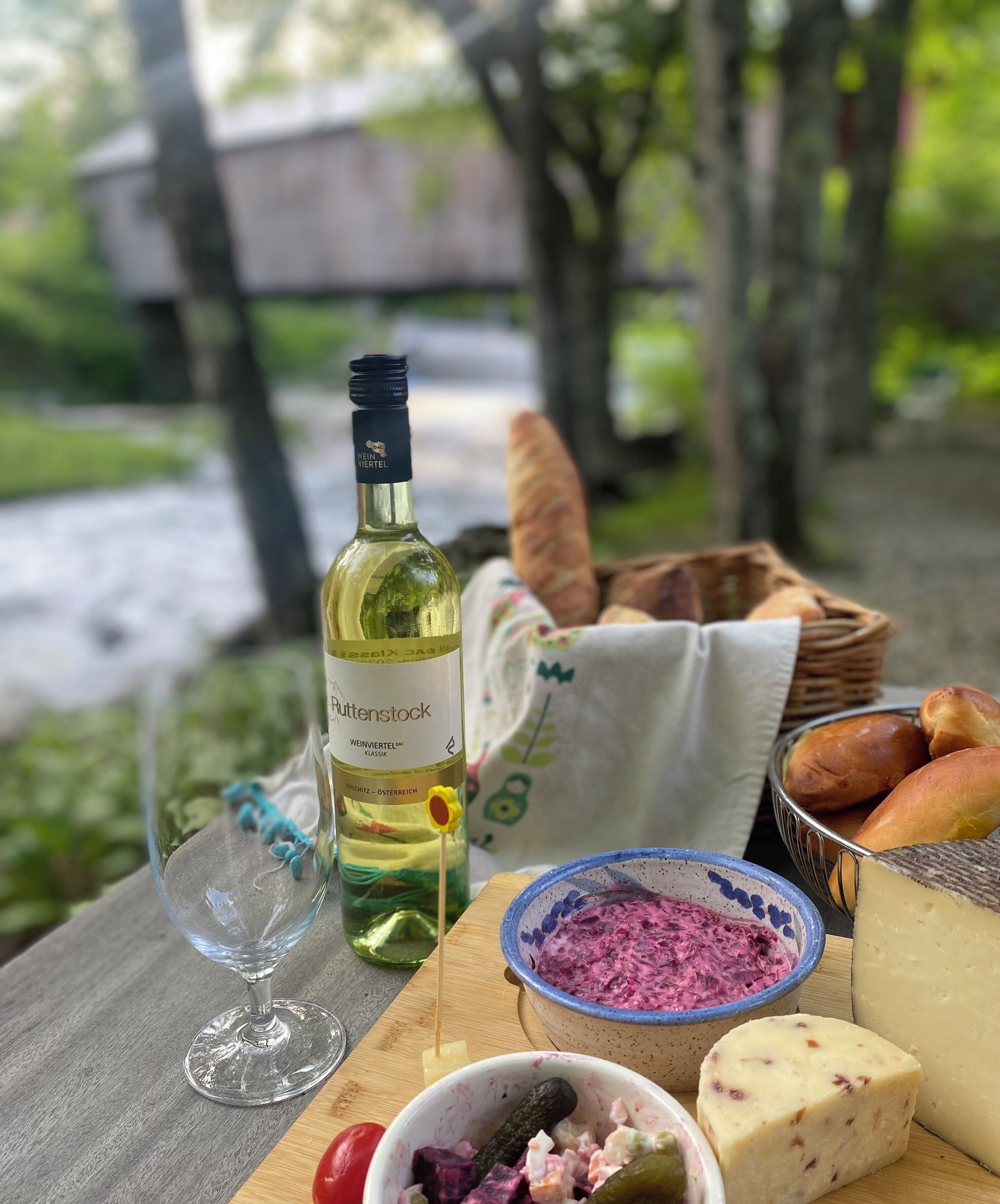 A table with a bottle of wine, a glass, a bowl of dip, cheese, and bread.